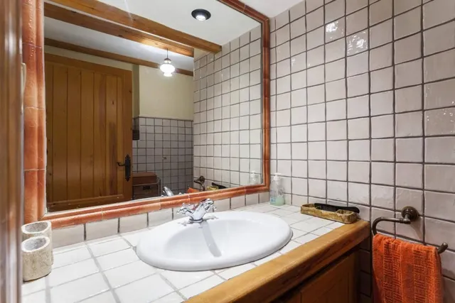 Aseo con encimera alicatada en blanco, lavabo ovalado y espejo con marco de madera junto al toallero