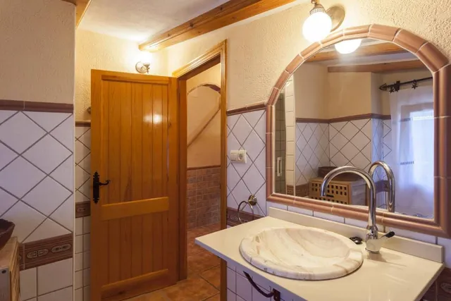 Aseo con lavabo tallado en piedra, espejo enmarcado en barro cocido y aplique de latón sobre el mueble