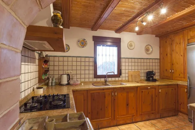 Cocina en L con encimera de granito, fogones de gas, campana extractora, hervidor y cafetera bajo techo de cañizo