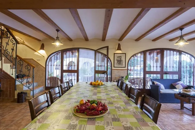 El comedor desde la cabecera de la mesa, con la escalera de forja a la izquierda y los ventanales en arco abiertos al porche