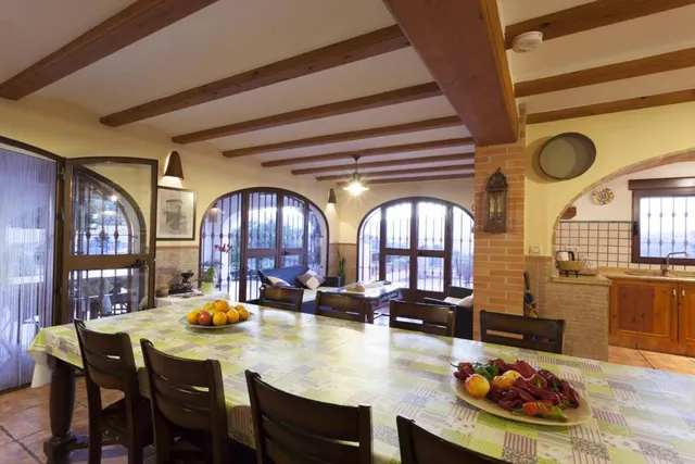 Comedor con mesa larga para diez, abierto a la cocina y con tres ventanales en arco hacia la terraza