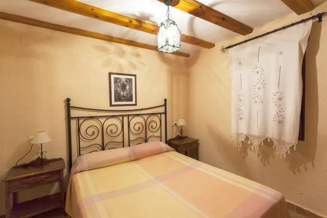 El dormitorio crema visto de lado, con el farol de forja del techo y la ventana vestida con visillo bordado a mano