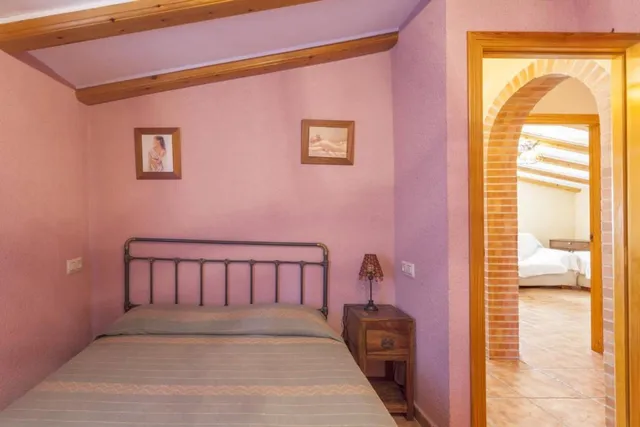 Dormitorio de paredes rosa empolvado con cama de matrimonio, cabecero de barrotes de hierro y arco de ladrillo a la estancia contigua