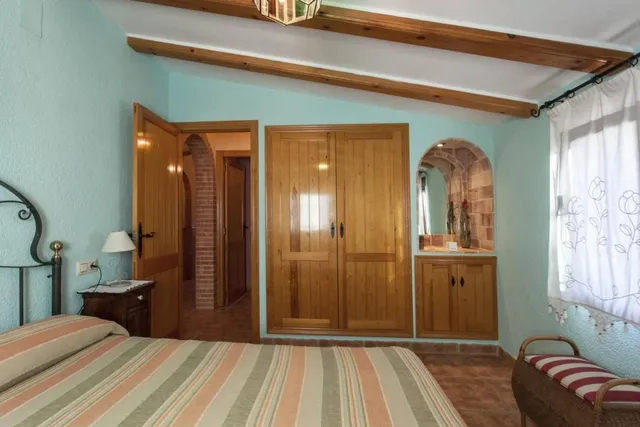 Armario empotrado de madera y hornacina con espejo en el dormitorio verde agua, con banqueta de mimbre junto a la ventana