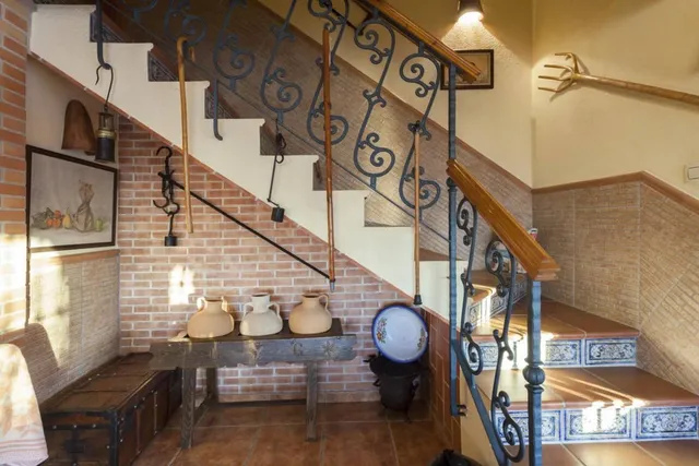 Escalera de peldaños de barro con azulejo pintado a mano, barandilla de forja y cántaros de cerámica bajo el tiro