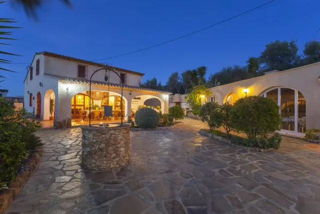 La villa iluminada al anochecer, con el pozo de piedra en el centro del patio empedrado y el porche encendido