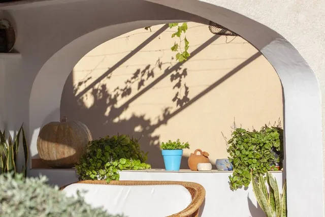 Detalle del arco del porche, con la sombra de la parra dibujada sobre la pared encalada y macetas alineadas en el poyete