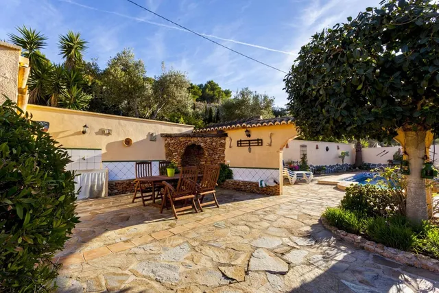Patio empedrado con comedor exterior y la piscina asomando al fondo, junto al anexo cubierto con teja