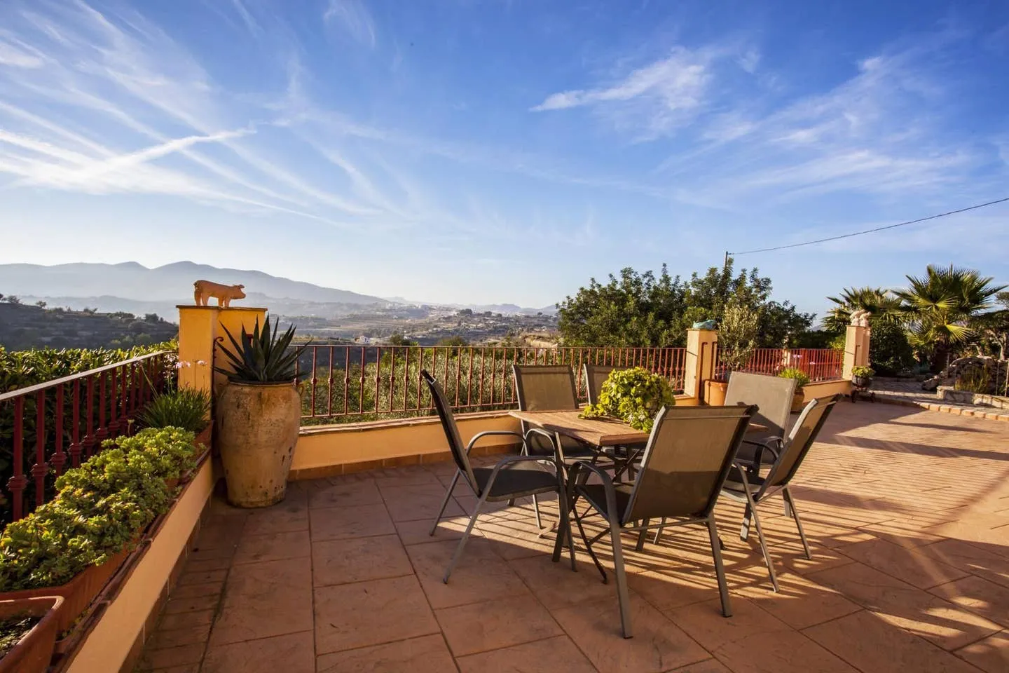 Terraza alta con mesa y sillas de jardín, macetones de barro y vistas abiertas al valle y a la sierra